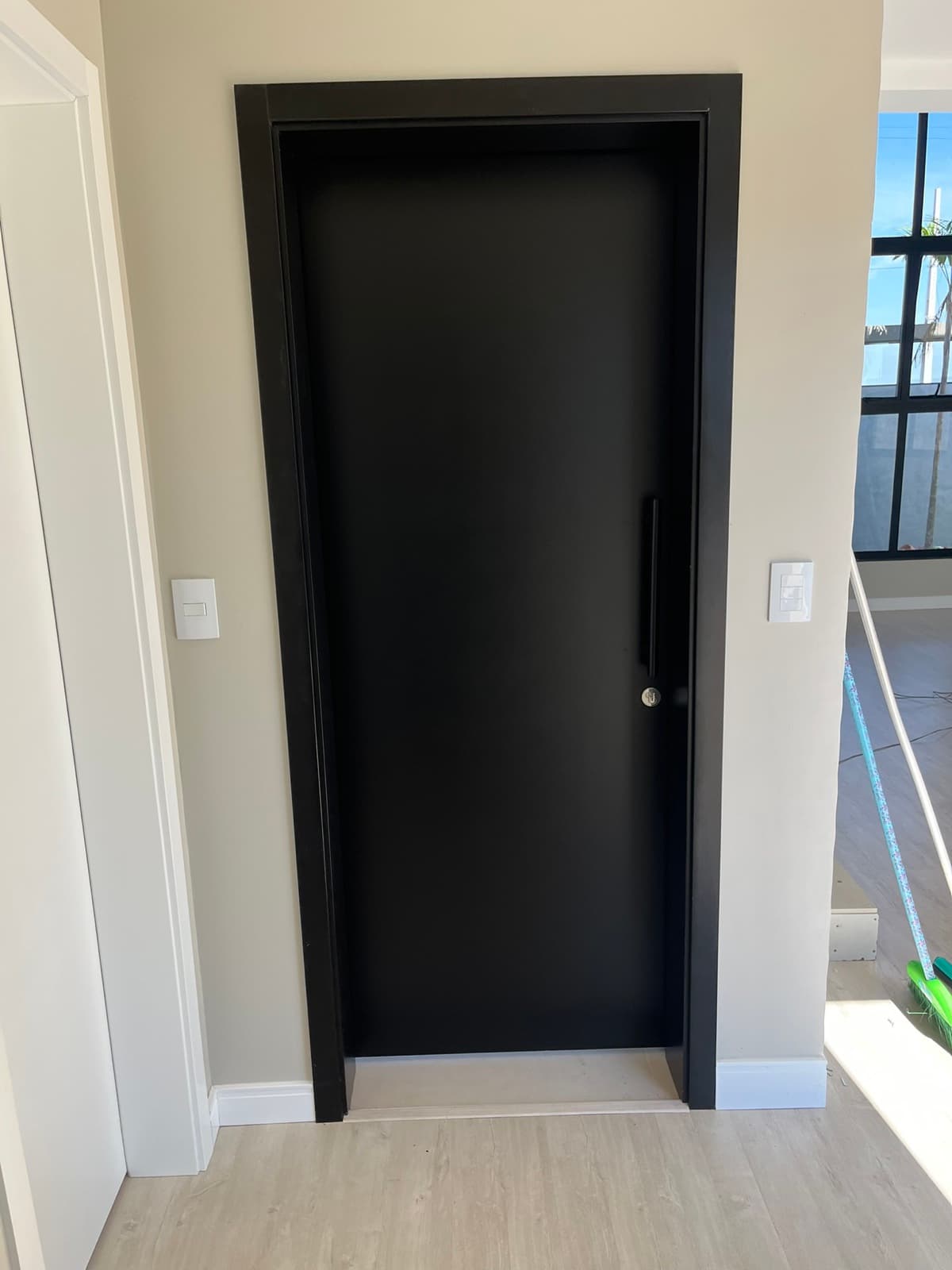 Ambiente interno com porta preta, piso claro e rodapé branco